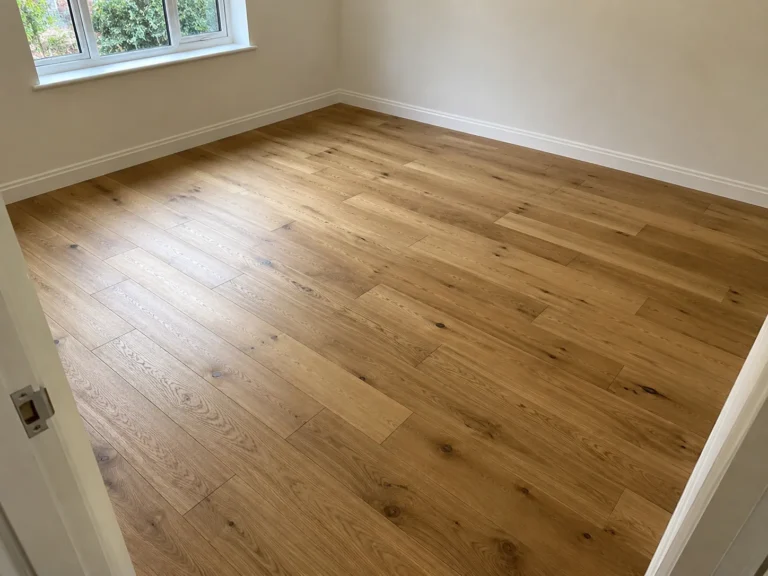 newly laid oak plank flooring in an empty room with white skirting boards and a window